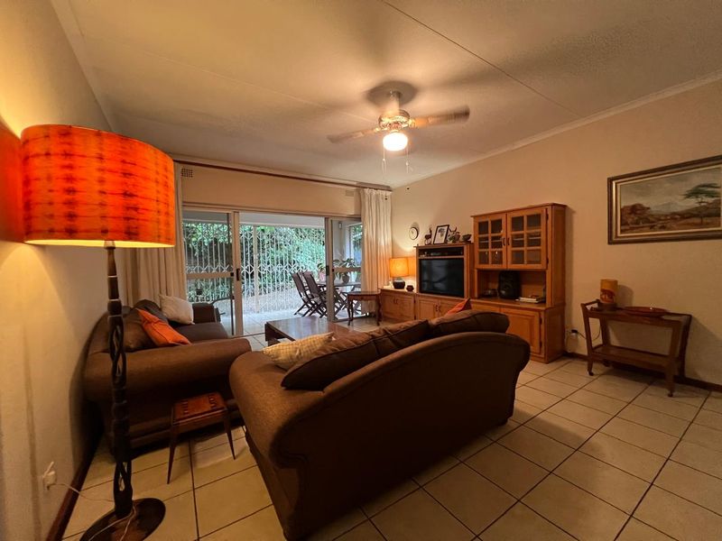 A comfortable living room featuring tiled flooring, a ceiling fan, and large sliding glass doors that provide access to an outdoor patio area.