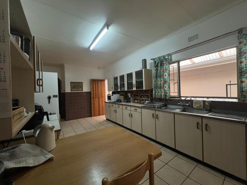A functional kitchen featuring extensive built-in cabinetry, laminate countertops, a double stainless steel sink, and tiled flooring with a neutral color palette.