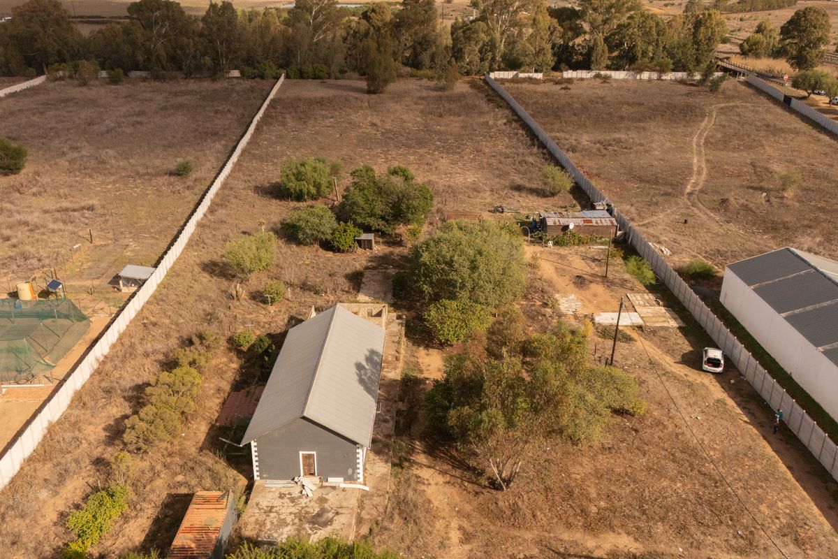 Aerial view of a large residential vacant land plot featuring a small existing structure, perimeter fencing, and established trees.