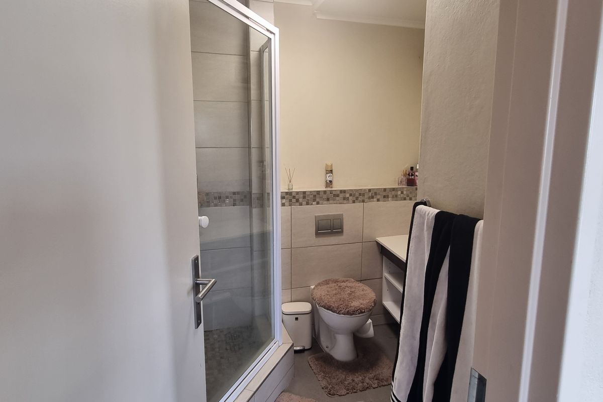 A functional bathroom featuring a glass shower enclosure, wall-mounted toilet, and a vanity cabinet with neutral wall tiling.