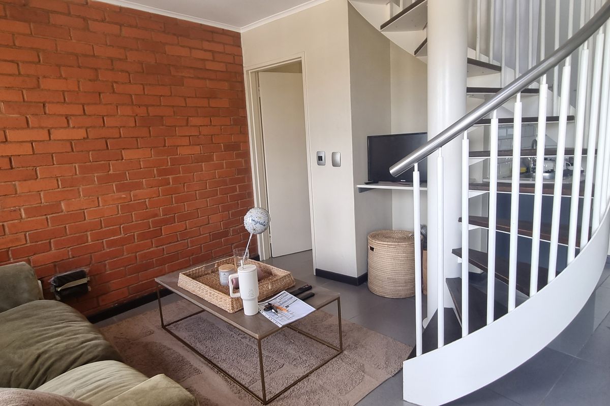 Living area featuring an exposed brick feature wall and a modern spiral staircase with a metal handrail.