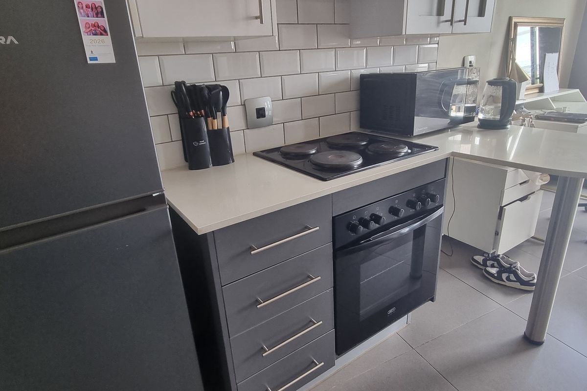 Modern kitchen featuring grey cabinetry, quartz countertops, subway tile backsplash, and integrated electric hob and oven with an attached breakfast bar.