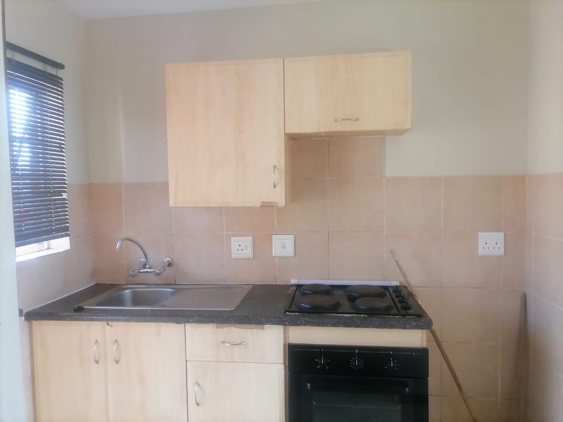 A functional kitchen featuring light wood cabinetry, a stainless steel sink, and a built-in electric oven and hob with tiled splashback.