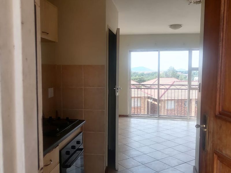 An open-plan kitchen and living area featuring tiled floors, built-in oven and hob, and a sliding door leading to a balcony with scenic views.