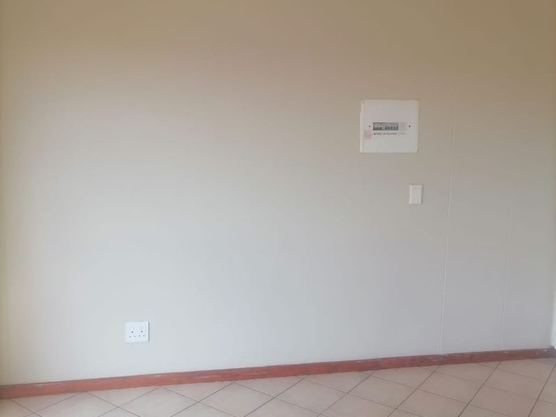 An empty living area featuring neutral wall paint, tiled flooring, and a wall-mounted electrical distribution board.