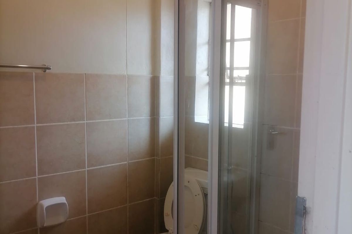 A functional bathroom featuring a shower enclosure, toilet, and neutral wall and floor tiling.