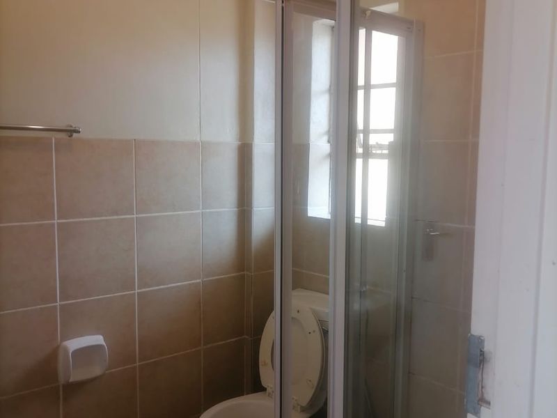 A functional bathroom featuring a shower enclosure, toilet, and neutral wall and floor tiling.