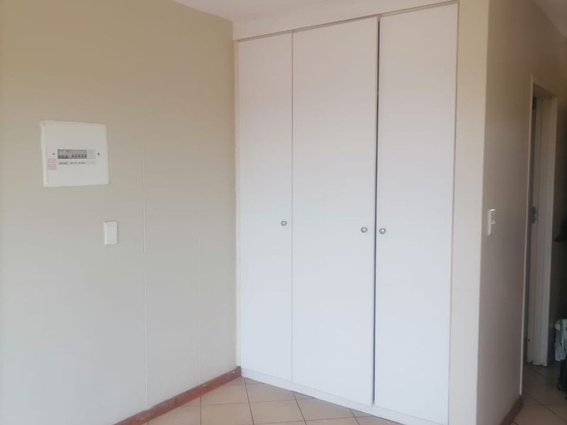 A clean, empty bedroom featuring neutral walls, tiled flooring, and a built-in white wardrobe with ample storage space.