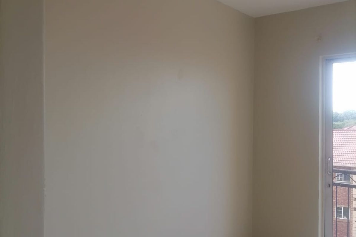 An empty bedroom featuring tiled flooring, neutral walls, and a sliding glass door providing access to a balcony.