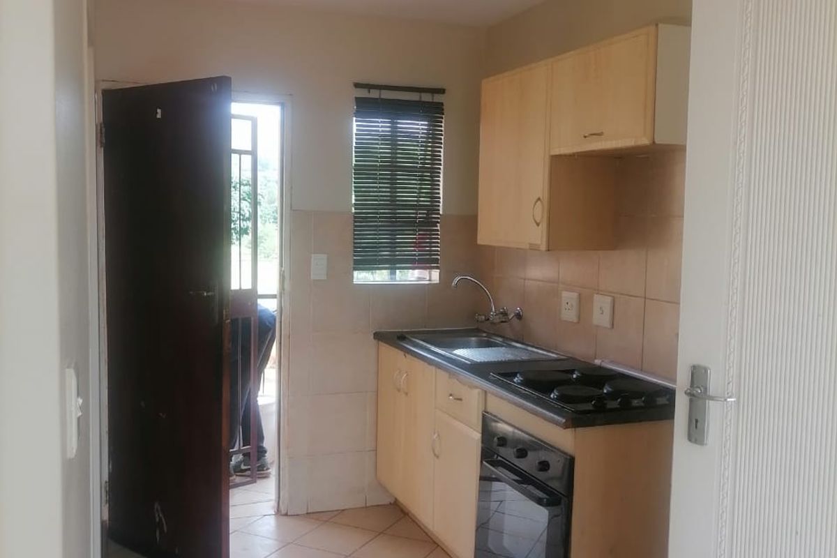 A compact kitchen featuring built-in cabinetry, a built-in oven and hob, tiled backsplash, and tiled flooring, with direct access to an exterior area.
