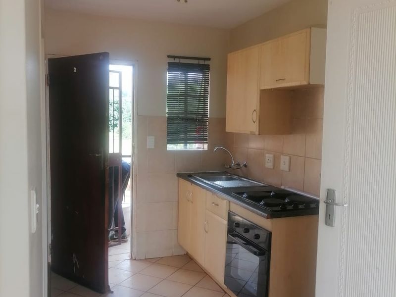 A compact kitchen featuring built-in cabinetry, a built-in oven and hob, tiled backsplash, and tiled flooring, with direct access to an exterior area.