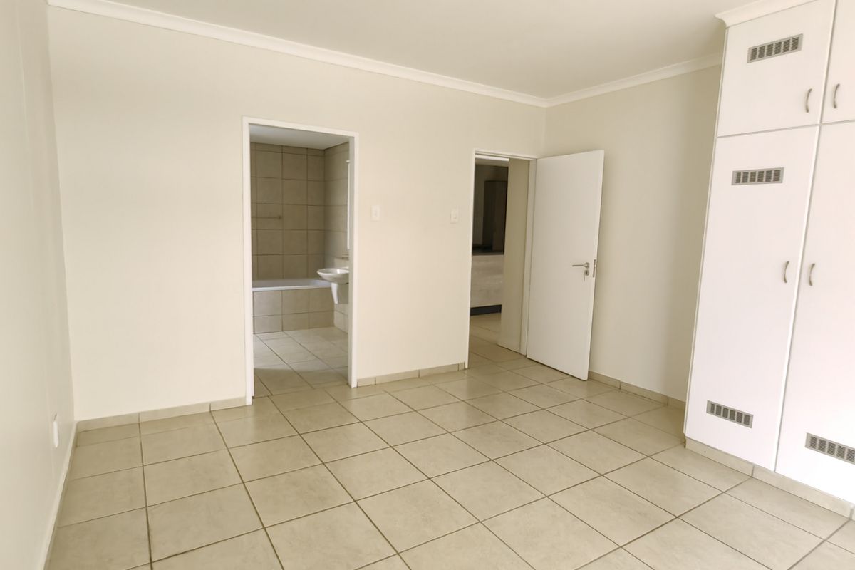 A bright, empty bedroom featuring neutral floor tiles, built-in cupboards, and direct access to an en-suite bathroom.