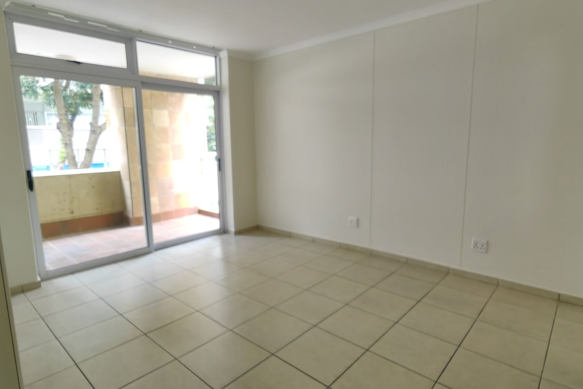 An empty living room featuring tiled flooring and a large sliding glass door providing access to an outdoor balcony area.