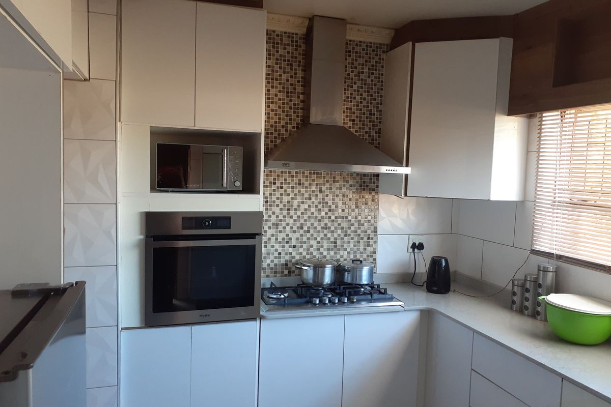 A functional kitchen featuring built-in cabinetry, a stainless steel extractor fan, a gas hob, and a wall-mounted oven with an integrated microwave.
