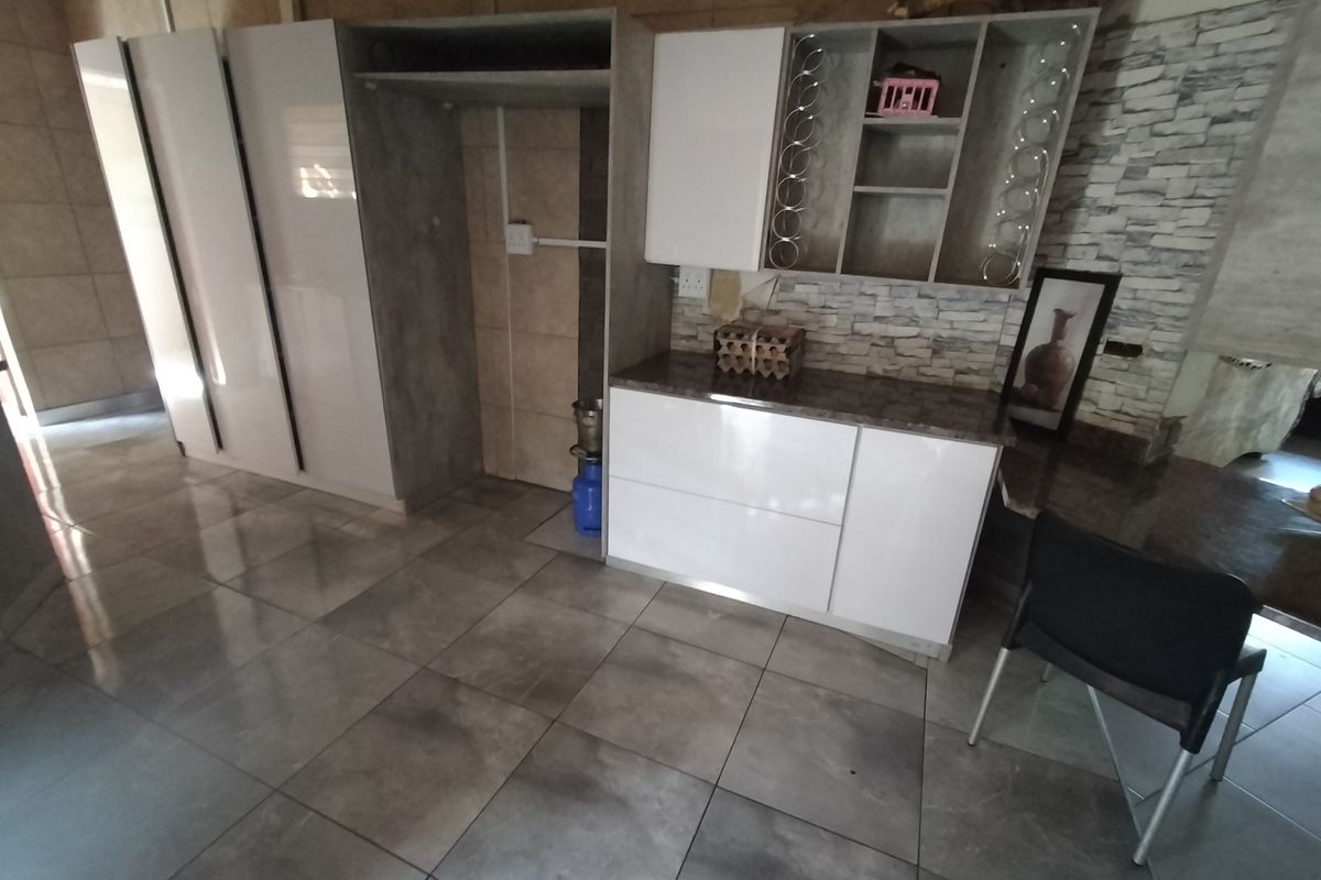 A modern kitchen area featuring sleek white cabinetry, stone-look wall accents, and large format floor tiles.