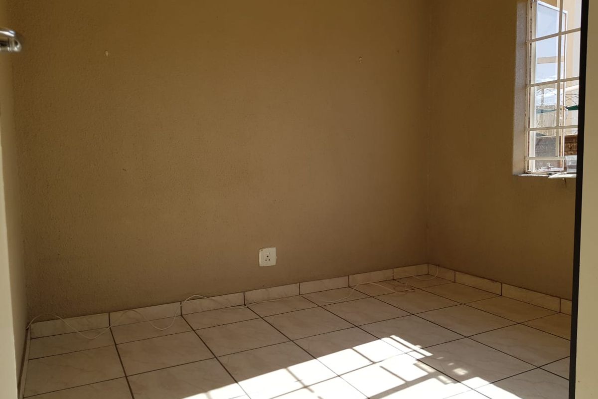 An empty bedroom featuring tiled flooring, a window with security bars, and neutral wall finishes, ready for personalization.