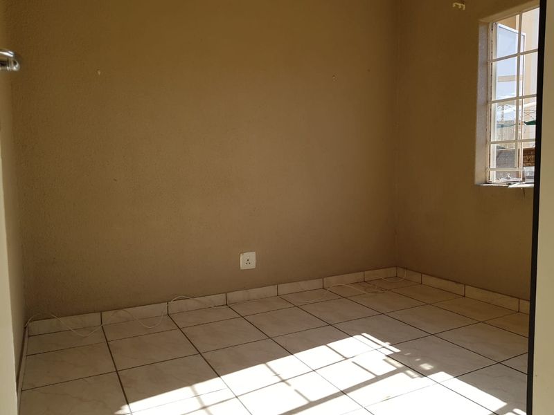 An empty bedroom featuring tiled flooring, a window with security bars, and neutral wall finishes, ready for personalization.