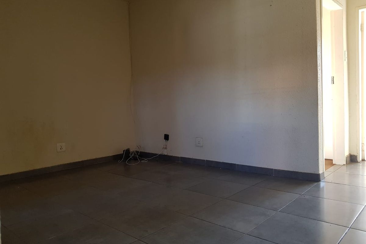 An empty living room featuring neutral tiled flooring and plain walls, offering a blank canvas for personalization.