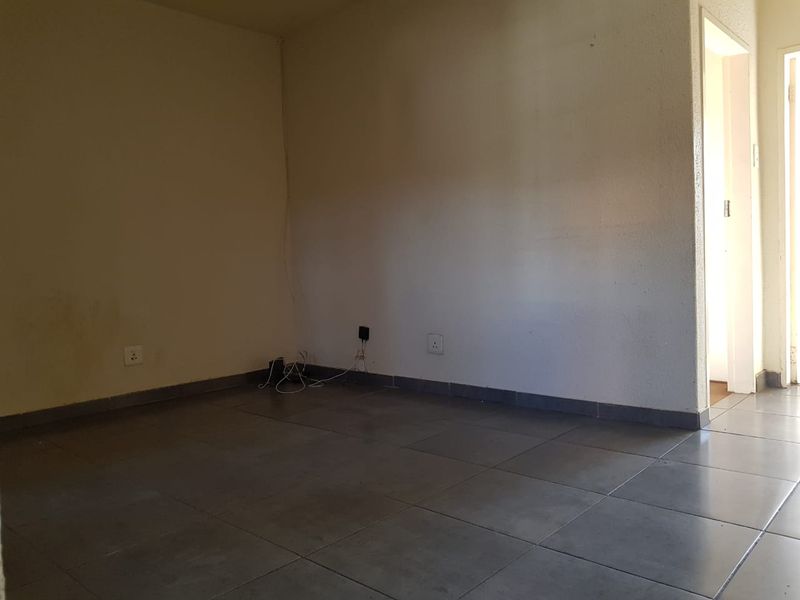 An empty living room featuring neutral tiled flooring and plain walls, offering a blank canvas for personalization.
