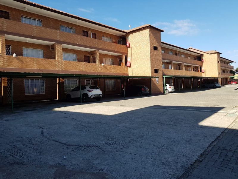Exterior view of a multi-story brick apartment complex featuring covered parking bays and a concrete driveway.