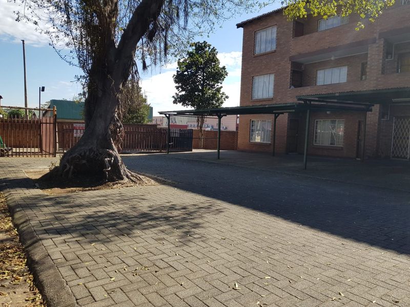 Exterior view of an apartment building featuring a brick facade, paved driveway, and covered carport parking area.