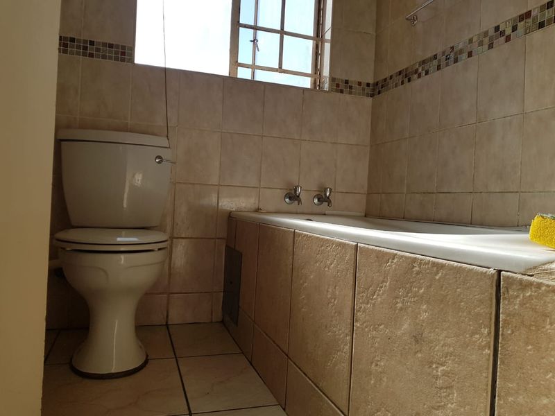 A dated bathroom featuring a standard toilet and bathtub with tiled walls and flooring, requiring cosmetic updates to improve its overall appeal.