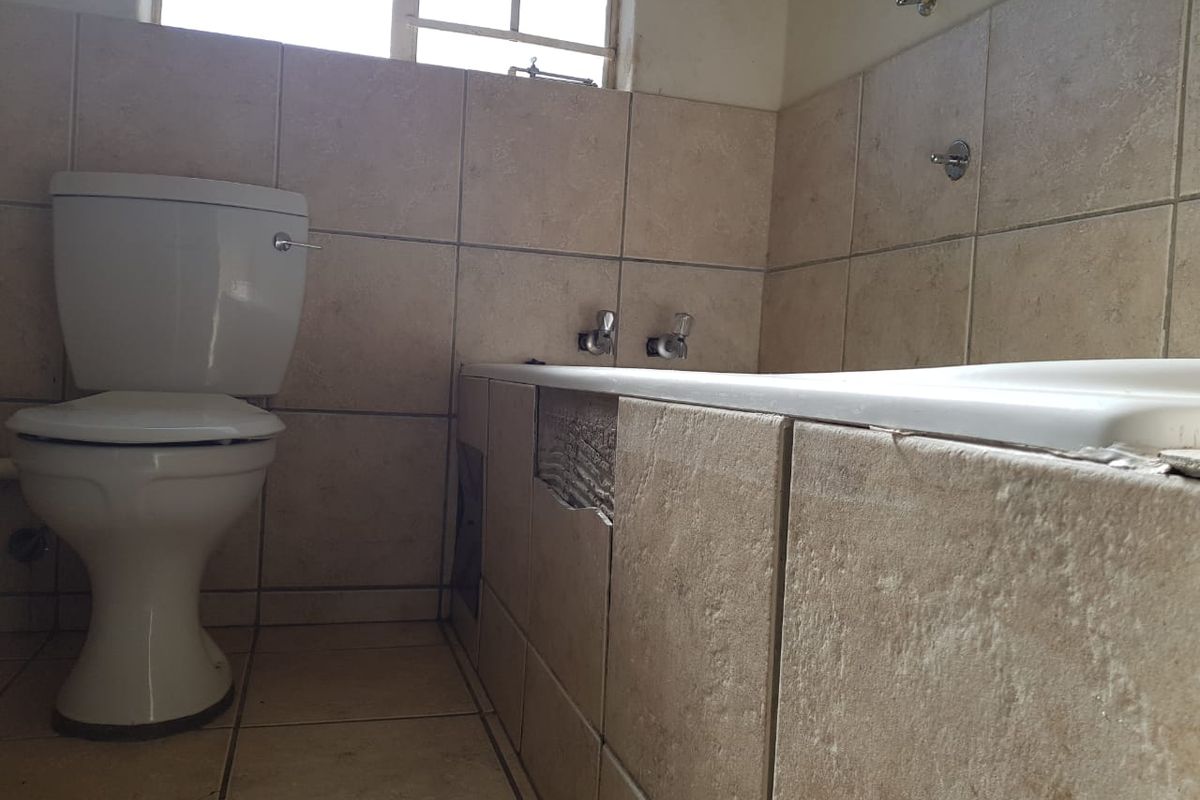 A bathroom featuring a toilet and bathtub with tiled finishes, currently requiring repairs to the bathtub apron and general maintenance.