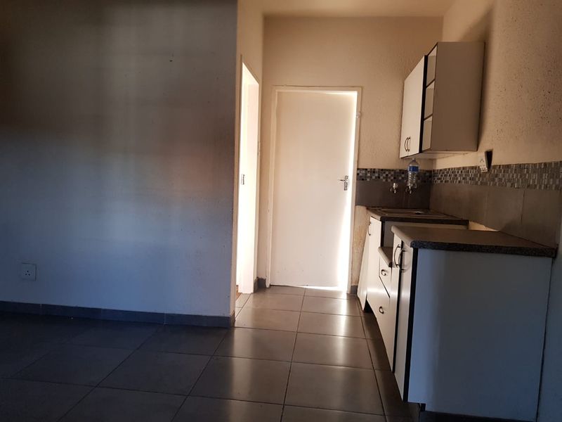 A compact, empty kitchen area featuring basic cabinetry, tiled backsplash, and tiled flooring, requiring cosmetic updates to improve its overall appeal.