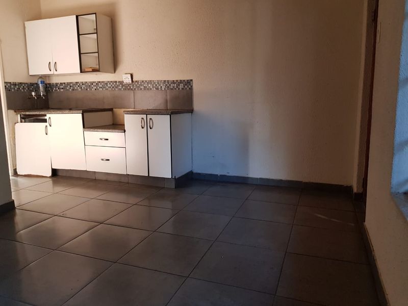 A compact kitchen area featuring tiled flooring, mosaic backsplash, and built-in cabinetry, currently requiring minor repairs and cosmetic updates.