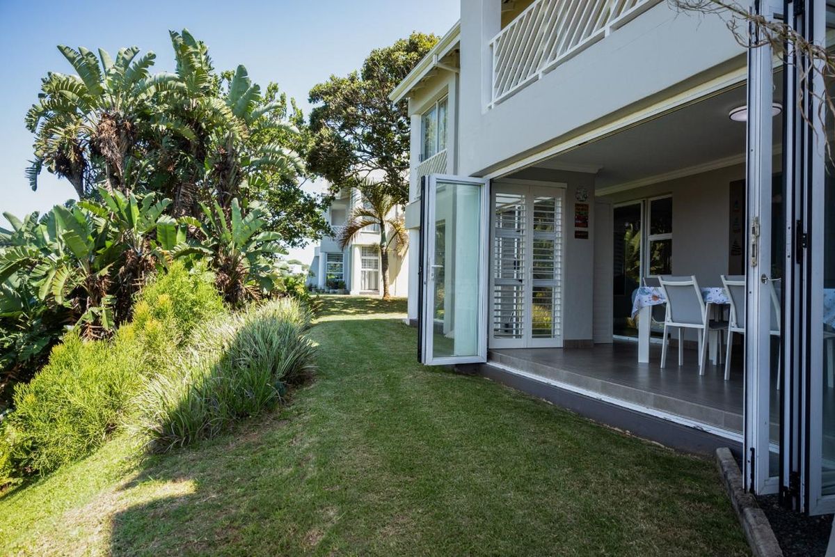 Rear view of the apartment featuring a landscaped garden, a tiled patio area, and large bi-fold doors leading into the living space.