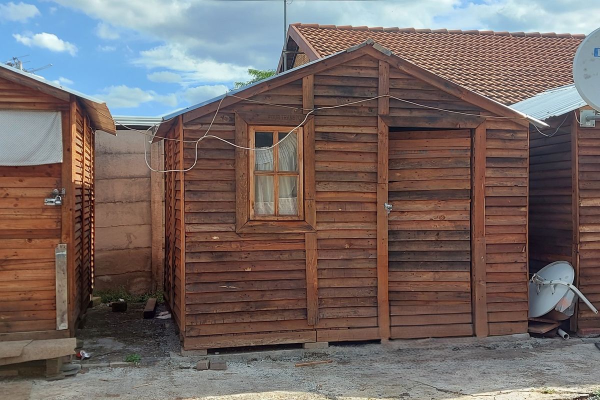 A detached timber structure with a tiled roof, featuring wooden cladding and a single window, situated in an outdoor area.