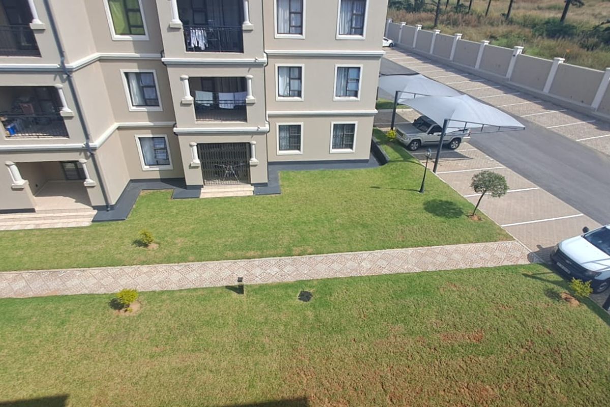 Aerial view of the apartment complex exterior, featuring landscaped lawns, paved walkways, and covered parking bays.