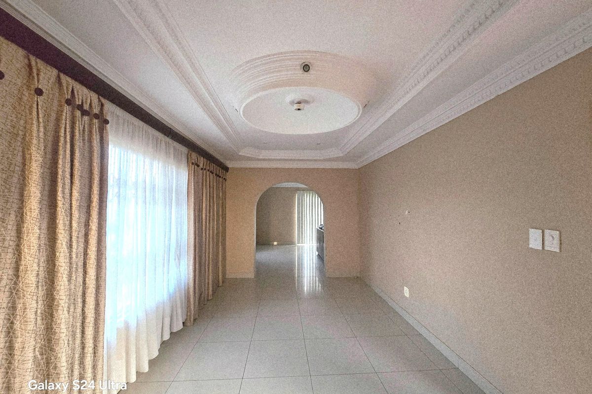 An empty living room featuring tiled flooring, an ornate ceiling rose, and a decorative archway leading to an adjacent space.
