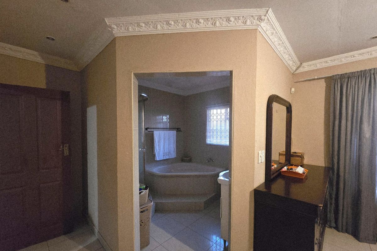 En-suite bathroom featuring a corner bathtub and built-in vanity, accessed from the bedroom area with decorative ceiling cornicing.