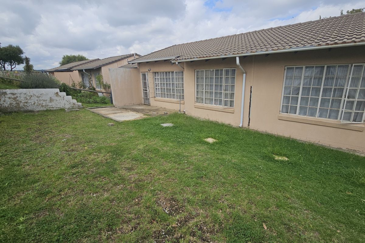 Rear view of the townhouse featuring a concrete patio, grid windows, and a private garden area with established lawn.