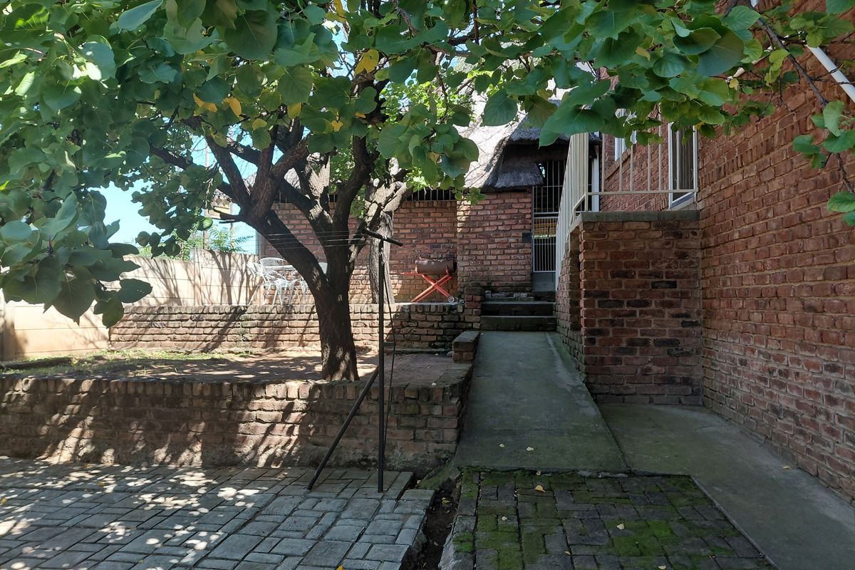 A rear exterior view of the property featuring exposed brick walls, a paved walkway, and a mature tree in the garden area.