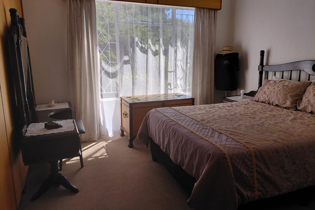 A well-lit bedroom featuring neutral carpeting, built-in cabinetry, and a large window with security bars, offering a comfortable and functional living space.