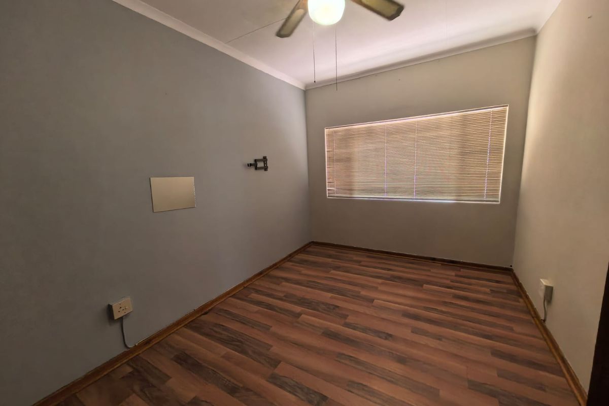 An empty bedroom featuring laminate flooring, a ceiling fan, and venetian blinds, providing a neutral blank canvas for potential residents.