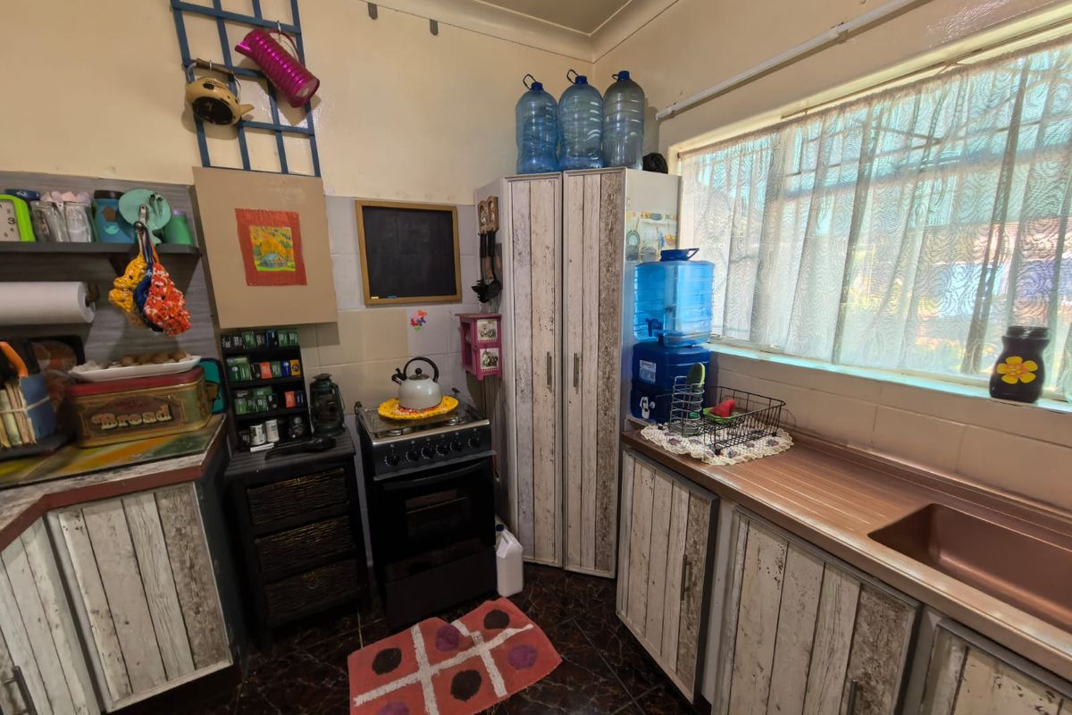 A compact kitchen featuring built-in cabinetry, laminate countertops, a stainless steel sink, and a freestanding stove with tiled backsplash and flooring.