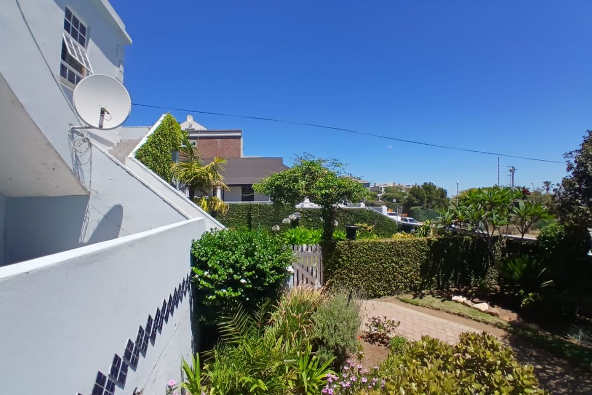 A view of the rear exterior area featuring a landscaped garden, paved pathway, and established hedging, viewed from an elevated balcony.