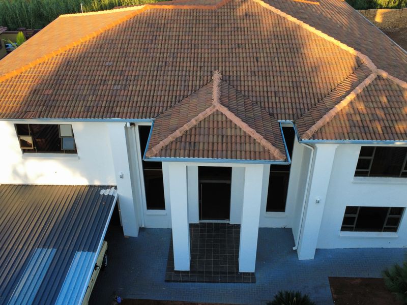 Aerial view of a two-story residential property featuring a tiled roof, white exterior walls, and a paved driveway with an attached carport.