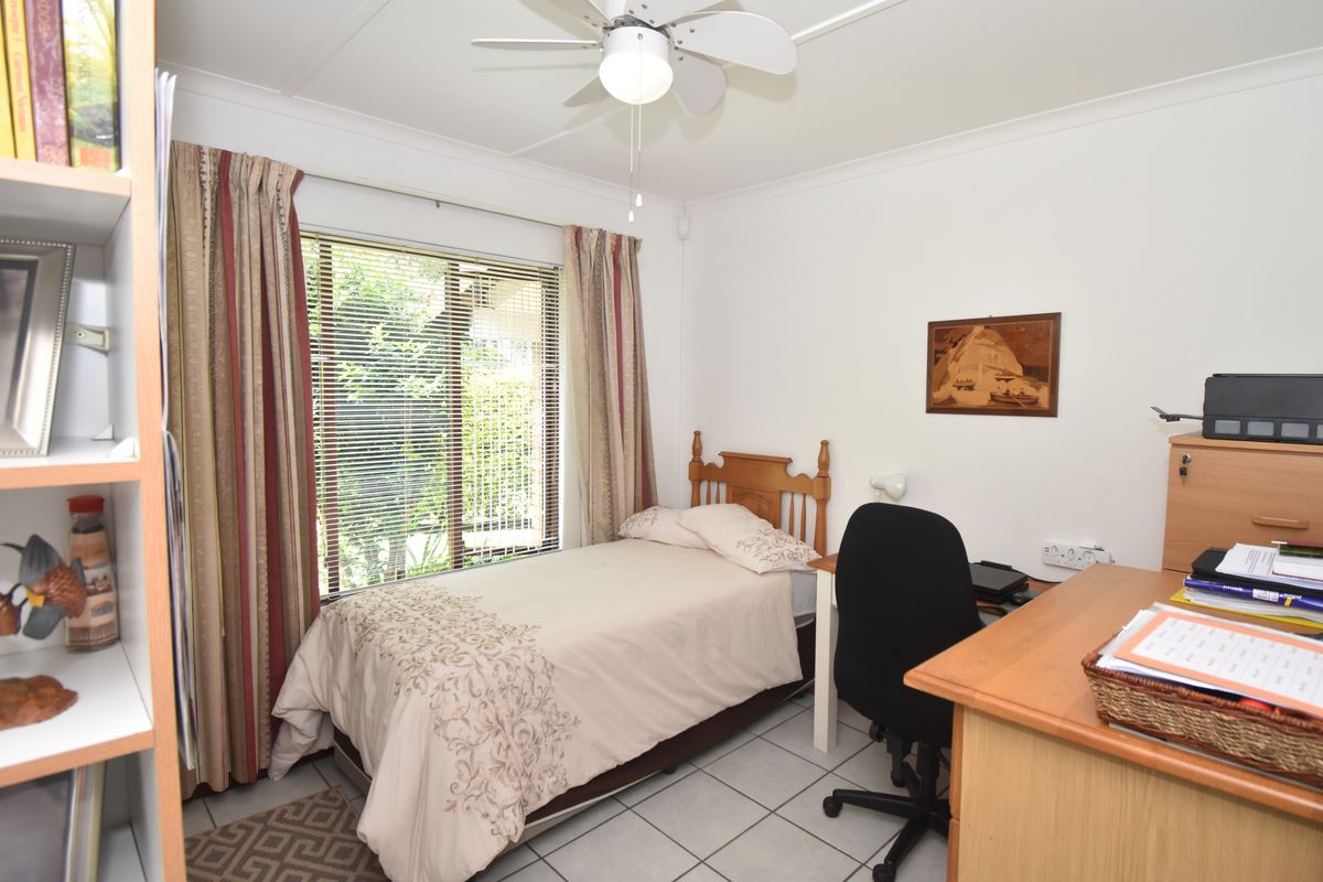A functional bedroom featuring tiled flooring, a ceiling fan, and large windows with blinds, offering a comfortable space for rest or study.