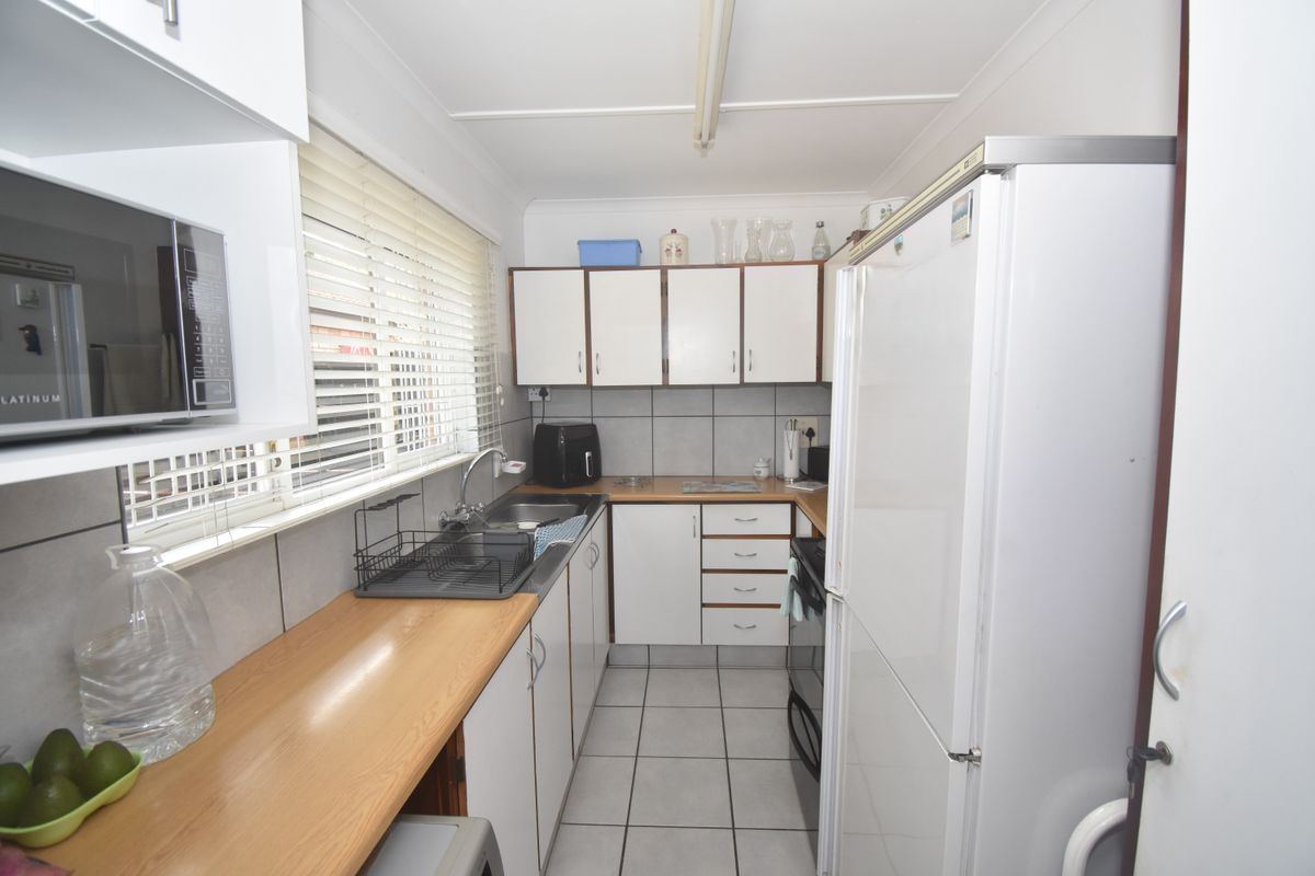 A functional galley-style kitchen featuring white cabinetry, laminate countertops, tiled backsplash, and tiled flooring, offering a practical layout for daily meal preparation.