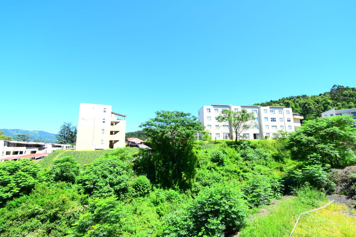 A wide-angle view of multi-story apartment buildings situated on a lush, green hillside under a clear blue sky.