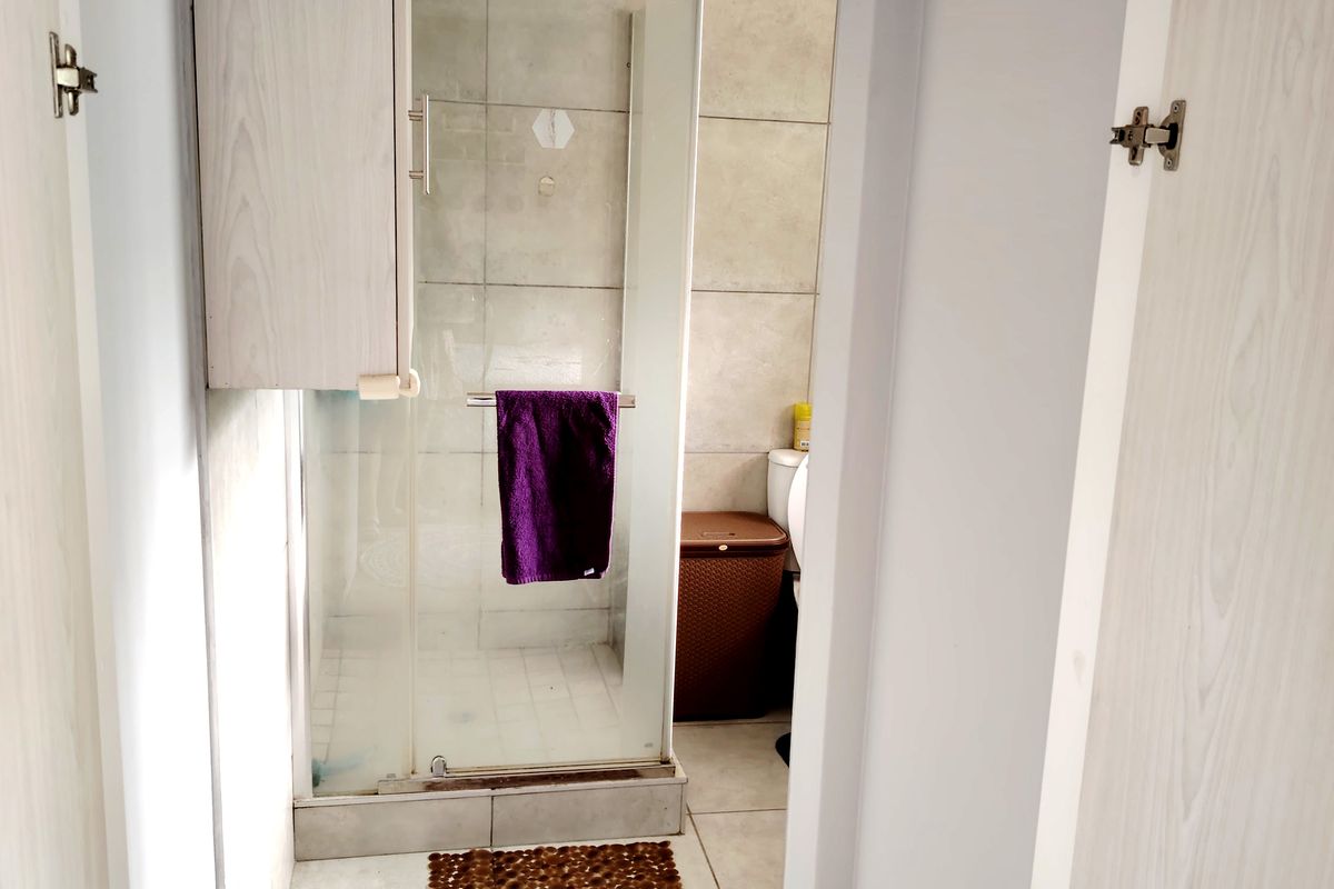 A functional bathroom featuring a glass shower enclosure, neutral wall and floor tiling, and a built-in storage cabinet.