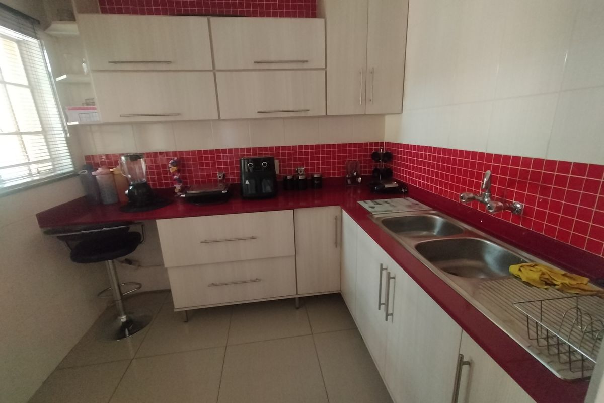 A functional kitchen featuring light-toned cabinetry, a contrasting red tiled splashback, laminate countertops, and a double bowl stainless steel sink.
