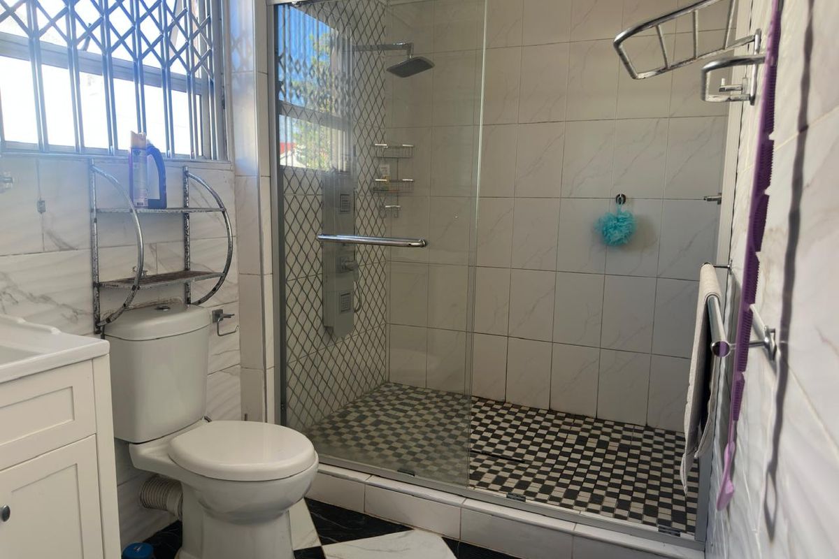A functional bathroom featuring a glass-enclosed shower with a rainfall showerhead, a white vanity, and a toilet, finished with marble-look wall tiles.