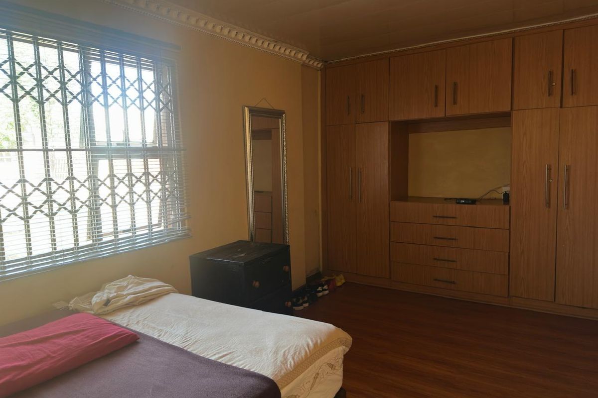A bedroom featuring built-in wooden cabinetry, laminate flooring, and a window fitted with security bars.