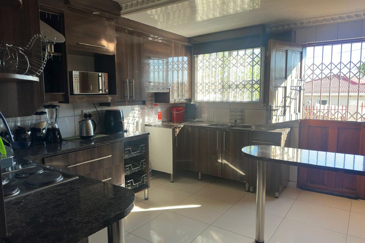 A functional kitchen featuring dark wood-look cabinetry, granite-style countertops, a built-in hob, and tiled flooring with direct access to the exterior.
