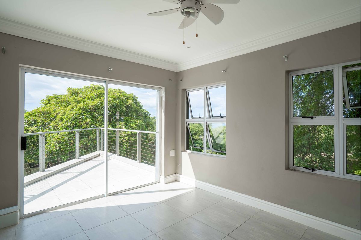Bright and spacious living area featuring neutral tiled floors, crown molding, a ceiling fan, and large sliding doors opening onto a private balcony.